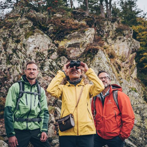 Drei Personen schauen mit eine Fernglas bei einer Wanderung in die Ferne.
